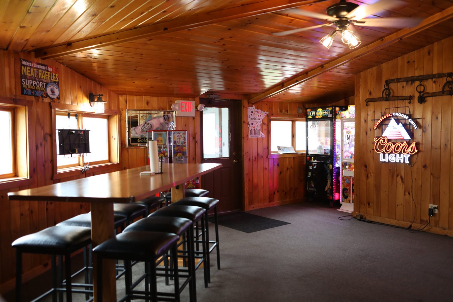 Inside Mudflats: knotty pine walls and ceiling, a long high-top table with stools, claw machines, and a Coors Light neon sign