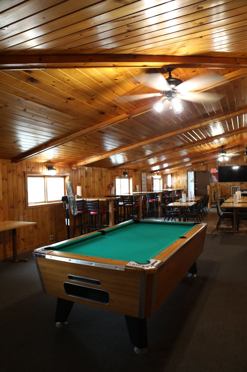 The pool table under the pine ceiling, with the bar seating beyond